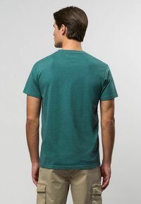 Teal kortärmad t-shirt tillverkad av mjuk bomull, med rund hals och lös passform. Slät textur med minimal märkning på baksidan.