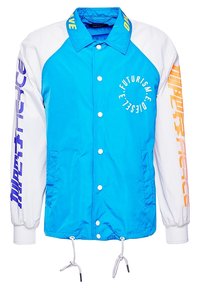 Modrá a bílá bunda s patentkami, stahovací pas a grafickým textem na rukávech. Disponuje hladkým, lehkým polyesterovým materiálem.