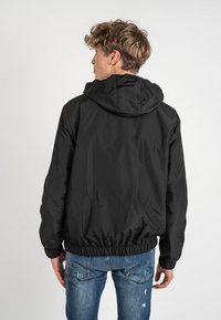 Giacca bomber nera con cappuccio, dotata di polsini e orlo elasticizzati, realizzata in un materiale leggero e morbido, progettata per una vestibilità comoda.