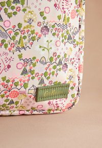 Többszínű textil táska, virág- és tájmintával, zöld részletekkel és hímzett logócímkével. Puha, tartós anyag.