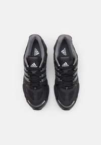 Svarta sportskor med meshovverdel, texturerade ytor och tre silverränder. Har grå accenter och en vadderad krage.