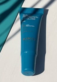 Tyrkis leppomai tube med ribbet hette, merket "Solbeskyttende leppomade," med hvit og gull tekst, som måler omtrent 10 cm lang.