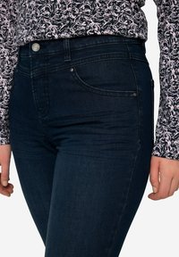 Jeans de mezclilla azul oscuro con cintura alta, detalles de bolsillo visibles y una textura ligeramente cepillada. La tela tiene un acabado suave.