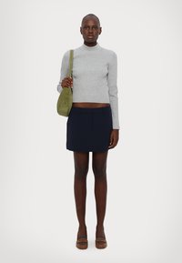 Maglione grigio a coste maniche lunghe, minigonna blu navy, borsa a tracolla verde, mocassini marroni con cinturini. Tessuto morbido e silhouette aderente.