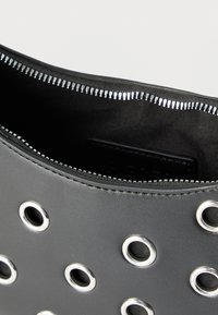 Μαύρη τσάντα από συνθετικό δέρμα με ασημένιες μεταλλικές τρύπες και μερικώς ανοιχτό ασημένιο φερμουάρ που αποκαλύπτει μαύρο υφασμάτινο εσωτερικό.