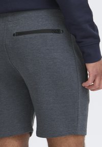 Graue Sportshorts mit glatter Textur, ausgestattet mit einer Gesäßtasche mit schwarzem Reißverschluss und dezenten Nähdetails.
