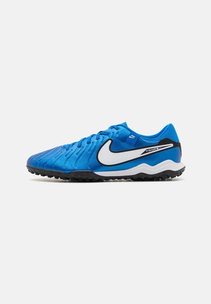 Chaussure de football Nike Tiempo bleue avec logo blanc, semelle noire et dessus texturé pour jeu sur gazon synthétique, présentée sur un fond uni.