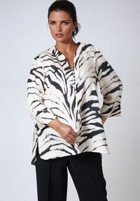 Wit en zwart gestreepte blouse met een V-hals, knoopdetail aan de voorkant, driekwartmouwen en zijsplitten; lichtgewicht stof.