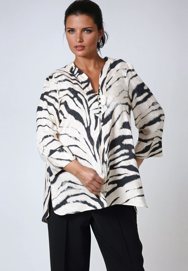 Blouse rayée blanche et noire avec un décolleté en V, des boutons à l'avant, des manches trois-quarts et des fentes sur les côtés ; tissu léger.