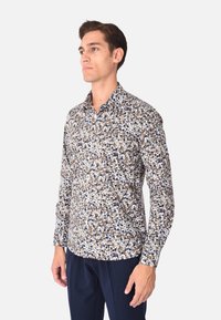 Camicia leggera con bottone in avanti, caratterizzata da un motivo astratto di punti multicolori in tonalità di blu, marrone e crema. Maniche lunghe con colletto a punta.