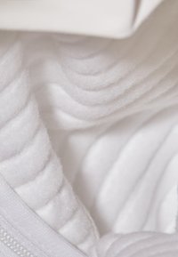 White fabric with textured, wavy patterns. Soft, fluffy material with sheen. Includes a zipper along the edge, creating a layered appearance.