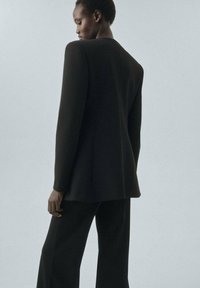 Black blazer with structured shoulders, tailored fit, and notch lapels, paired with matching wide-leg pants. Smooth fabric texture.