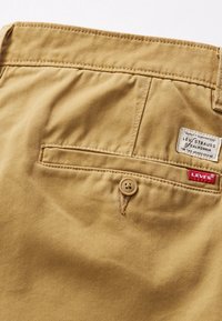 Pantalon en coton beige avec poche arrière à fermeture bouton et deux étiquettes de la marque Levi's cousues au-dessus de la poche du côté droit.