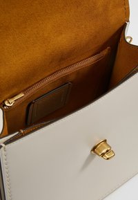 Beige läderväska inuti med en slät yta, utrustad med en gyllene tryckknappsstängning, brunt mockafoder och en ficka med dragkedja.