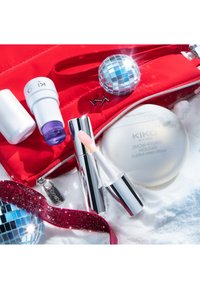 Röd nylon kosmetikpouch med silverdetaljer, assorterade kosmetika inklusive en klar handkräm, läppglans och en dekorativ discokula.