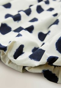 Baumwollstoff mit weißem Hintergrund und großen marineblauen abstrakten Punkten, der eine weiche Textur und gefaltete Abschnitte aufweist.