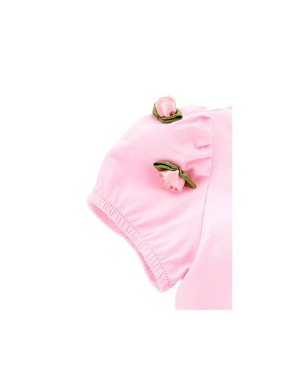 Grembiule rosa a maniche corte con polsini elastici, decorato con due rose di tessuto e foglie verdi. Texture liscia.