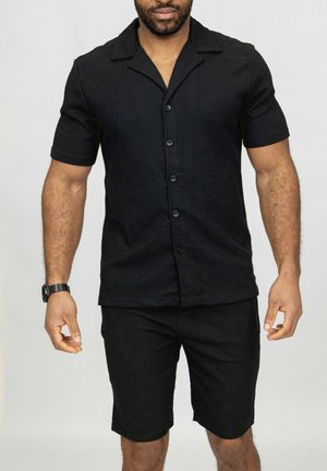 Chemise noire à manches courtes avec col, ornée d'une fermeture à boutons à l'avant, assortie à un short noir en tissu texturé.