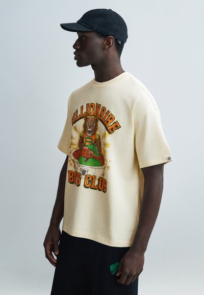 Cream oversized t-shirt with a graphic print featuring a bear and bold text, paired with black shorts displaying a green logo.