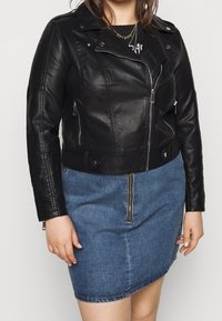 Veste de moto en cuir noir avec des poches zippées et un col à pression, portée sur une jupe en denim bleu avec une fermeture éclair à l'avant et un ourlet légèrement asymétrique.