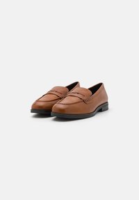 Mocasines de cuero marrón con punta redondeada, que presentan un detalle de costura elevada y suelas planas de goma negra para mayor agarre y comodidad.