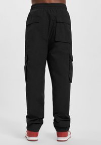 Schwarze Cargo-Hosen mit elastischem Bund, ausgestattet mit Seitentaschen und Gesäßtaschen. Der Stoff ist glatt und leicht, entworfen für Komfort.