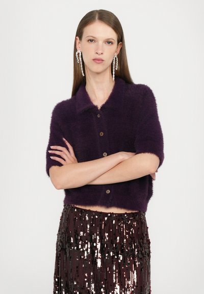 Kurzer lila, flauschiger Cropped-Cardigan mit Kragen und vier braunen Knöpfen, kombiniert mit einem paillettenbesetzten burgunderfarbenen Rock.