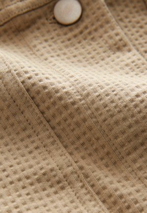 Waffle-patterned beige fabric with visible texture, featuring a light-colored button and stitched seams, showcasing its soft, woven appearance.