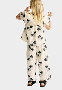 Blouse courte à manches courtes beige clair et pantalons larges imprimés floraux noirs. L'ensemble présente une coupe décontractée et une texture douce. Sandales noires.