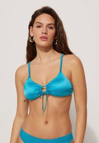 Haut de bikini turquoise avec un détail en trou de serrure, de fines bretelles réglables et une texture froncée. Matériau lisse semblable à du satin.