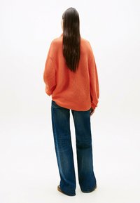 Maglione arancione oversize lavorato a maglia con maniche lunghe, abbinato a jeans in denim blu larghi. Texture morbida, vestibilità rilassata e gamba ampia.
