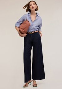 Vaaleansininen nappikauluspaita, tummat leveälahkeiset farkut, vaaleanruskea vyö kultaisilla yksityiskohdilla, teksturoitu vaaleanpunainen laukku ja vihreillä yksityiskohdilla varustetut sandaalit.