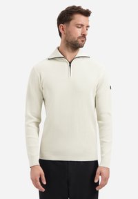 Lichtcrème geribbelde pullover met een half-rits kraag, lange mouwen en een zwarte accent op de linkermouw. Zachte textuur en aansluitend ontwerp.