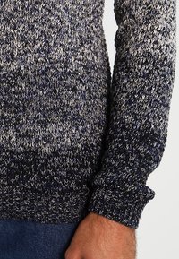 Gestrickter Pullover in Marineblau mit hellgrauen und weißen Sprenkeln. Verfügt über gepolsterte Bündchen und ein strukturiertes Muster in entspannter Passform.