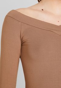 Brun off-the-shoulder långärmad topp i mjukt, ribbat material. Har en V-formad halsringning och slät textur.