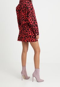 Röd och svart leopardmönstrad skjortklänning med lös passform och fransad nederkant; kombinerad med ljuslila ankelstövlar med hög klack och sidoremsa.