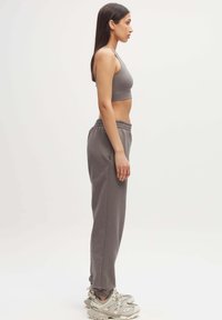 Grijze sportbeha met dunne bandjes, gedragen met high-waisted grijze joggingbroek. Sneakers met lichte accenten en chunky ontwerp. Over het geheel een gladde textuur.