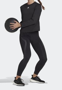 Svart långärmad träningsskjorta och högmidjade leggings med reflekterande detaljer, matchat med svarta träningsskor, hållande en svart medicinboll.