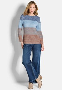 Maglioncino a righe in tonalità blu e marrone, lavorato a maglia leggera, colletto tondo, maniche lunghe. Abbinato a jeans a gamba larga blu e stivaletti beige.