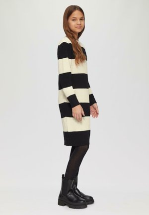 Gebreid jurkje met zwart en crème horizontale strepen, lange mouwen en een rechte snit, gecombineerd met chunky zwarte enkellaarzen.