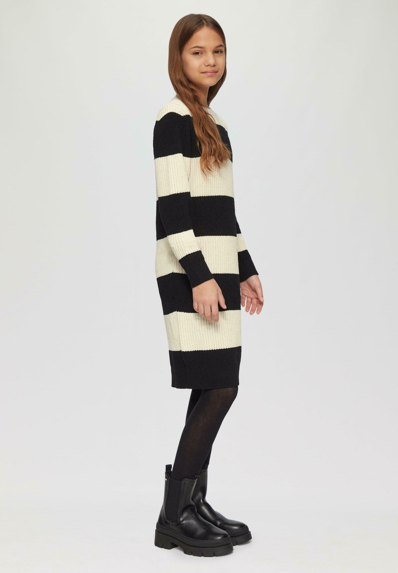 Gebreid jurkje met zwart en crème horizontale strepen, lange mouwen en een rechte snit, gecombineerd met chunky zwarte enkellaarzen.