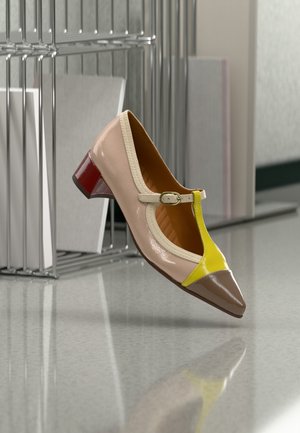 Μπεζ δερμάτινο παπούτσι με κίτρινες και καφέ λεπτομέρειες, σχέδιο T-λουριού, μικρό κόκκινο τακούνι και κομμένη πλευρά. Υφασμάτινη υφή στα λουριά.