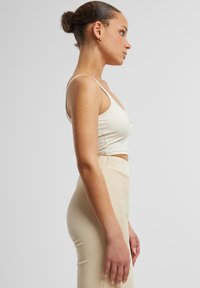 Béžový skrátený top s tenkými ramienkami, skombinovaný s hladkou, vysokopásovou béžovou sukňou s rebrovanou štruktúrou. Hladká textúra látky s jemnými švami a krivkami.