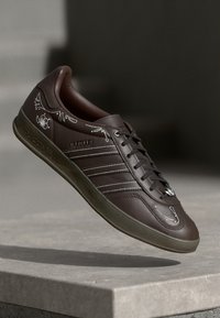 Bruine leren Adidas Gazelle sneaker met drie strepen, vetersluiting, gedetailleerde witte stiksels en een gestructureerde zool.