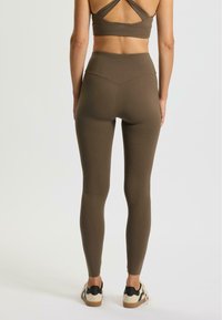 Bruine leggings met hoge taille gemaakt van rekbaar materiaal, met een naadloos ontwerp en een platte tailleband, gecombineerd met casual schoenen.