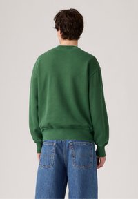 Groene sweatshirt met een relaxed fit, geribbelde mouwen en tailleband. Gecombineerd met blauwe denim jeans met achterzakken en stiksels.