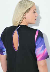 Camiseta negra de mangas cortas con un patrón abstracto en tonos morados y rosas, y un corte en forma de llavero en la parte posterior del escote.