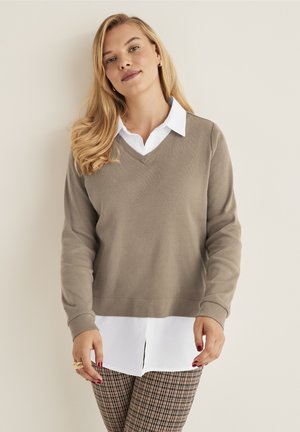 Beige V-hals trui met lange mouwen over een witte collared shirt; gestreepte bruine en witte geruite broek; gladde gebreide textuur.