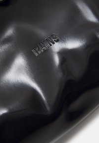 Čierna lesklá taška cez rameno vyrobená z vodoodolného materiálu. Obsahuje vyrazené logo "RAINS". Hladký povrch s elegantným, zaobleným tvarom.