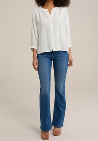 Valkoinen, kevyt nappipaita pitkähihaisilla hihoilla yhdistettynä viistosti leikkautuviin sinisiin farkkuculotteihin ja vaaleanruskeisiin korkokenkiin.